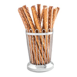 A bundle of long, salted pretzel rods stands upright in a stainless steel bread stick holder with a shiny, circular base. The golden-brown pretzels feature visible salt crystals, and the holder resembles a cylindrical cup or basket.