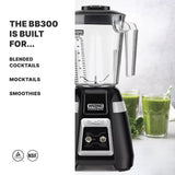 A Waring Commercial bar blender with a copolyester container is shown alongside two glasses of green smoothies. Text on the left reads: THE BB300 IS BUILT FOR... BLENDED COCKTAILS, MOCKTAILS, SMOOTHIES. Leafy greens sit nearby on a white surface.