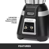 Close-up of a black Waring Commercial bar blender base. A label reads BLADE; two toggle switches—High/Low and PULSE—are visible. Text highlights a 1 HP Motor with 2-Speed Toggle Switch + Pulse. Compatible with stainless steel container. Bottom text says FEATURES.