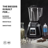 A professional bar blender (Waring BB320S) with a 1 HP motor and stainless steel container sits on a counter beside a glass bottle of milk, mini marshmallows, a squeeze bottle labeled “Gana 60%,” and chopped chocolate.