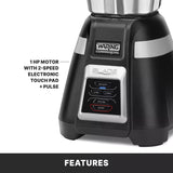 Close-up of a black Waring Commercial bar blender base. The control panel has labeled buttons: Low, High, Pulse, and Stop. Text notes “1 HP motor with 2-speed electronic touch pad + pulse.” Features label; compatible stainless steel container available.