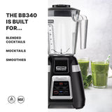 A powerful black Waring Commercial Bar Blender with a 1.4 liter copolyester container sits on a countertop beside two glasses of green smoothies and leafy greens. Text reads: “The BB340 is built for… blended cocktails, mocktails, smoothies.”.