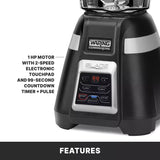 Close-up of a black Waring Commercial bar blender base with digital display showing 99, labeled buttons, and text highlighting its 1 HP motor, 2-speed electronic touchpad, 99-second countdown timer, and pulse function for international use.