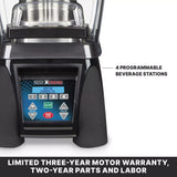 Close-up of a high-power blender’s control panel with four programmable beverage station buttons, speed, pulse, on/off, and start/stop. Text at the bottom highlights warranty and parts coverage. Shown with a durable stainless steel container.