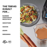A metal table holds a gray plate of salad with greens, grape tomatoes, croutons, and dressing. Next to it are raw carrots, a copolyester container of orange sauce on the TORQ 2.0 Series Blender—ideal for sauces and smoothies and ready for international use.