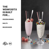 Two tall glass milkshakes sit on a metal surface. The left is pink with whipped cream, sprinkles, macarons, a straw, and spoon. The right is cookies and cream with candies. Text lists drinks the WDM120TX Heavy-Duty Drink Mixer can make.