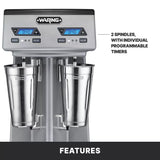 A Waring drink mixer with a double spindle and two metal mixing cups, each featuring individual programmable digital timers and speed/pulse controls, is shown on a gray and black background with labeled features.
