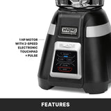 Close-up of a black Waring Commercial Blade Bar Blender base. The control panel features electronic touchpad controls labeled Off, Low, High, Pulse, and Stop. Text highlights the 1 HP motor with 2-speed touchpad + pulse. “Features” appears at the bottom.