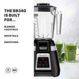 A black and silver Blade Bar Blender with a clear 48-oz. plastic container sits beside green smoothies and leafy greens on a white countertop. Text reads: The BB340 is built for blended cocktails, mocktails, smoothies. Certification icons below.