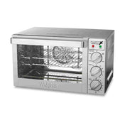 A stainless steel countertop oven with a clear glass door, wire rack, and three control knobs on the right for function, temperature, and timer. The brand Waring is visible on the front below the door.