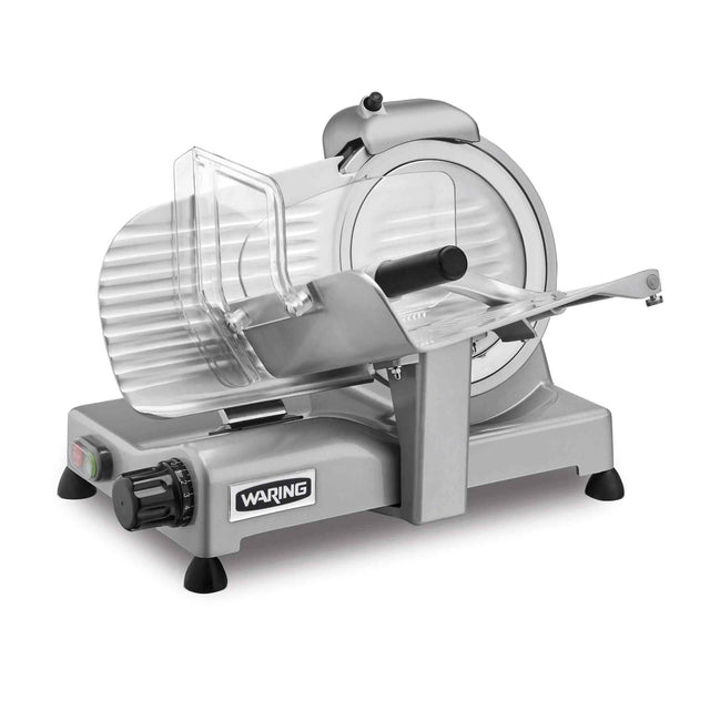 A silver electric food slicer with a circular serrated blade, transparent safety guard, and sliding tray. This Commercial Food Slicer features a black control knob for adjustable slice thickness and the “WARING” label on the side.