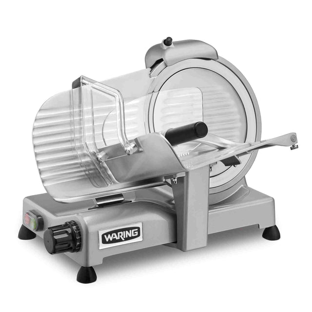 A silver electric food slicer with a circular blade, clear plastic guard, adjustable slice thickness dial, and “WARING” label on the front sits on four black rubber feet for stability against a white background.