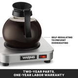 A glass coffee carafe filled with coffee sits on a stainless steel single burner Waring coffee warmer. Text points to the carafe, stating Self-regulating to prevent overheating. Below, a label reads, Two-year parts, one-year labor warranty.