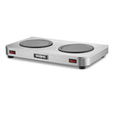 A stainless steel Waring double burner hot plate with two round heating elements, ideal as a coffee warmer, red power switches on each side, four black feet, and a central Waring logo on the smooth, modern front.