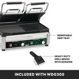 A stainless steel Commercial Panini Grill with two ridged plates is shown open. Labels point to its removable drip tray and a heavy-duty grill brush, both included with model WDG300. The front panel has switches and adjustable thermostats.