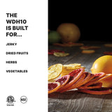 A wooden surface displays dried citrus slices, whole citrus fruits, and herbs. On the left, bold text reads: The WDH10 dehydrator is built for... Jerky, Dried Fruits, Herbs, Vegetables. Certification logos appear at the bottom left.