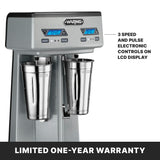 A silver heavy-duty double-spindle drink mixer with two stainless steel cups, twin LCD displays, and clearly labeled buttons for speed and pulse. Text highlights: “3 speed and pulse electronic controls on LCD.” Bottom: “Limited one-year warranty.”.