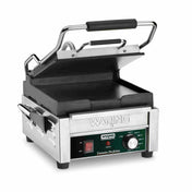 A compact toasting grill, this stainless steel Waring panini press features flat cast iron plates, a black handle, and a partially open top plate. The front panel offers adjustable thermostats, indicator lights, and the engraved Waring brand name.