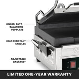 Close-up of a stainless steel compact toasting grill panini press with labels highlighting a hinged, auto-balancing top plate, flat cast iron plates, heat-resistant handles, and adjustable back feet. A black banner at the bottom states “LIMITED ONE-YEAR WARRANTY” in bold white text.