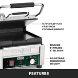 A stainless steel Waring Compact Toasting Grill with a raised lid, exposing 9.75x9.25 flat cast iron plates. Features an adjustable thermostat up to 570°F, brushed stainless steel body, and a control panel with labeled temperature settings.