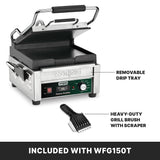 A Waring compact toasting grill with an open lid sits on a white background. Features are labeled: flat cast iron plates, a removable drip tray, and a heavy-duty grill brush with scraper. Text below reads, “Included with WFG150T.”.