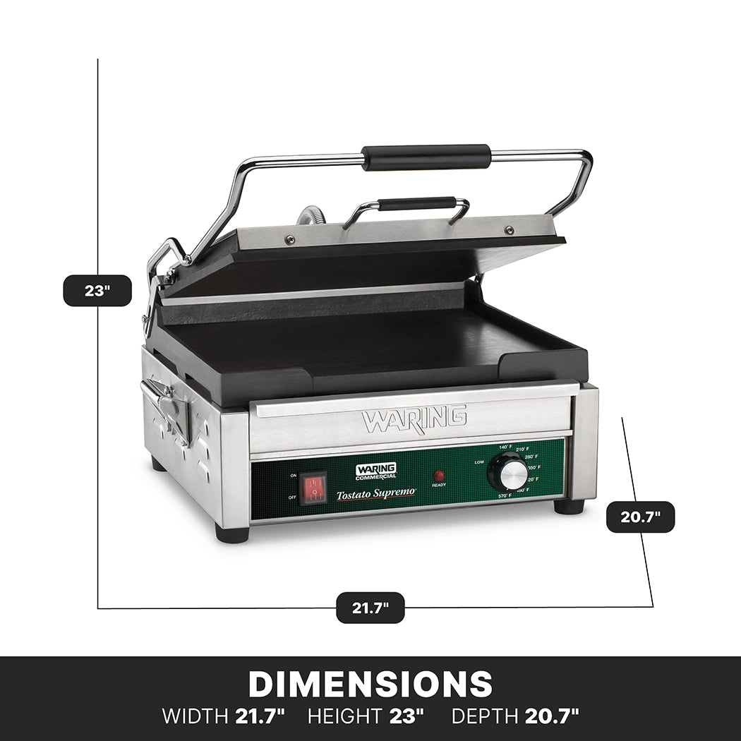 A stainless steel Waring commercial panini press sits open, revealing flat cast iron plates on both the top and bottom grill surfaces. The machine features a green control dial, labeled front panel, and adjustable thermostats for precise grilling. Measurements: width 21.7, height 23, depth 20.7.