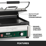 A Waring commercial panini press with cast iron plates, a 14.5 x 11 large toasting grill, brushed stainless steel body, and an adjustable thermostat up to 570°F. The slightly open press displays its interior surface with labeled feature text.