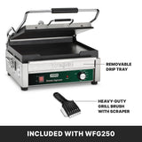 A stainless steel Panini Grill with a partially open lid, labeled Waring Toastio Supremo, sits on a black surface. To the right, text highlights an adjustable thermostat, removable drip tray, and grill brush shown in front of the press.