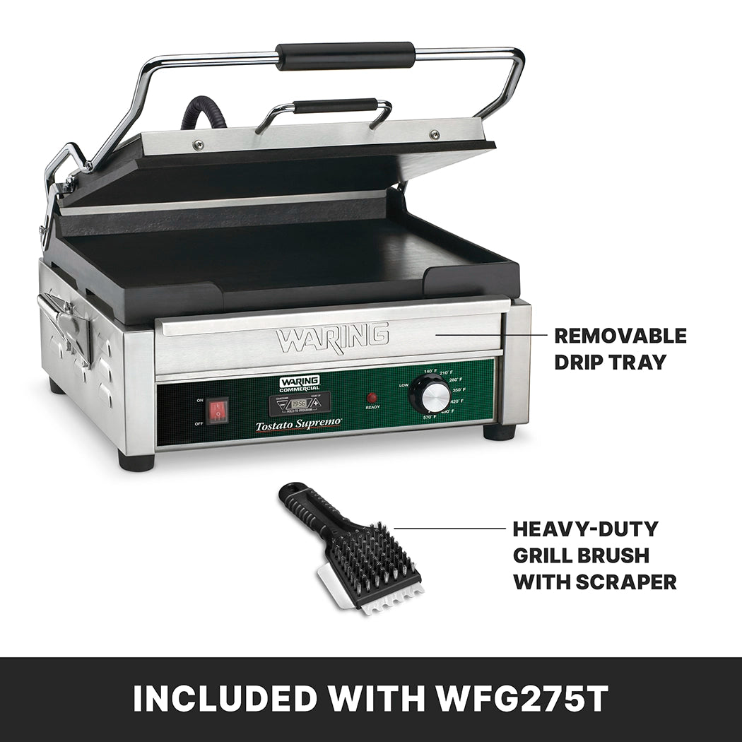 A stainless steel Panini Grill with a black grill plate and handle is shown partly open. Text points to a removable drip tray and a heavy-duty grill brush with scraper, both included with the WFG275T model.
