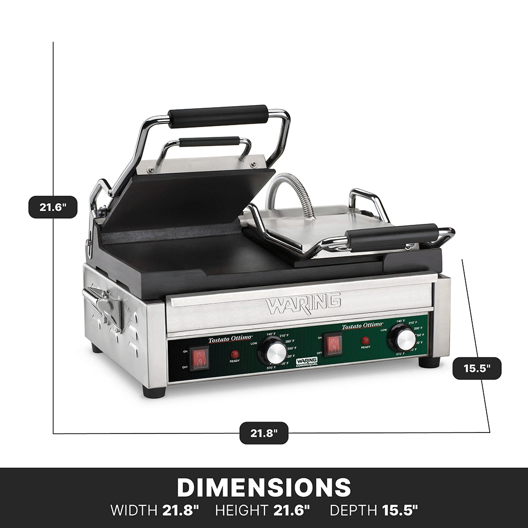 A stainless steel panini press with black handles is open, revealing ribbed cast iron plates. The dual toasting grill features adjustable thermostats, two control knobs, and indicator lights on a green front panel. Dimensions: 21.8”W x 21.6”H x 15.5”D.