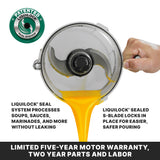 A hand tilts a batch bowl food processor, pouring yellow liquid. The bowl features an S-blade and patented LiquiLock Seal System. Text highlights the leak-proof processing and secure blade, with a warranty notice below.
