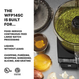 A batch bowl food processor containing green sauce sits on a counter next to a lid, a bowl of oil, a lemon, a cracked egg, and garlic. Text on the left lists features like large-batch and leak-free processing, plus chopping and puréeing.