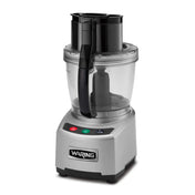 A silver Waring food processor with a clear 4 qt batch bowl and black handle. The base features three buttons: green, red, and black, with icons and text. The lid has a feed tube, pusher, and LiquiLock seal system. Waring logo on the front.