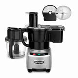 A silver and black Waring WFP16SCDE combination food processor with a clear batch bowl, black handle, lid, and feed chute. The base features three buttons: red, green, and yellow. Above, a circular slicing blade and grid attachment are shown separately.