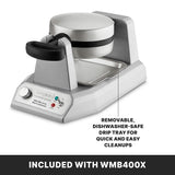 A silver heavy duty waffle maker with a black handle sits on a counter. It features non-stick waffle plates, a control knob, and an indicator light. A removable, dishwasher-safe drip tray is shown beneath it. Banner below reads: INCLUDED WITH WMB400X.