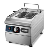 A stainless steel Waring WPC100K electric pasta cooker with two rectangular frying baskets, control knob, temperature dial, indicator light, and the brand name Waring on the front panel. The Pasta Cooker Rethermalizer sits on four short legs with a hinged lid behind the baskets.