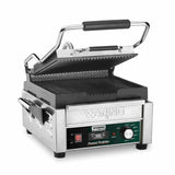 A stainless steel Waring commercial panini grill with ribbed cast iron plates, black handles, side utensil holder, temperature control knob, indicator lights, and an open, angled lid. The front displays branding and controls.