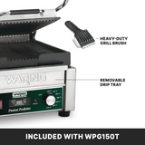 A compact panini grill with ribbed cast iron plates is shown with its lid open. Arrows highlight a heavy-duty grill brush above the grill and a removable drip tray below. A green control dial and indicator lights are visible. Text reads: “INCLUDED WITH WPG150T.”.