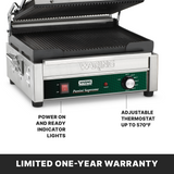 A stainless steel Waring panini grill with ribbed cast iron plates is shown. The front panel displays indicator lights labeled “POWER” and “READY,” plus a knob for the adjustable thermostat up to 570°F. Text highlights the warranty and product features.