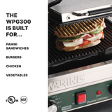 A close-up of a Waring Dual Panini Grill with ribbed cast iron plates grilling a sandwich with melted cheese, tomatoes, and greens. Text lists foods the WPG300 can cook: panini sandwiches, burgers, chicken, vegetables. Certification logos appear at bottom left.
