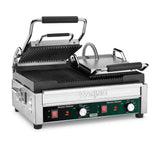 A stainless steel Waring WPG300 dual panini grill features a ridged top plate raised above the exposed bottom plate. The front panel includes controls, indicator lights, and labels, while black handles and a flexible metal cord are at the top.