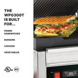 A grilled panini sandwich filled with sliced meat, cheese, tomato, and greens sits in an open Waring WPG300T dual panini grill. Text beside the image lists uses: panini sandwiches, burgers, chicken, vegetables. Certification logos are shown at the bottom.