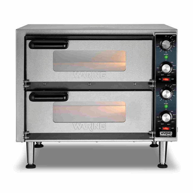 A stainless steel double-deck pizza oven with a ceramic pizza deck features two glass-windowed doors, black handles, and four control knobs on the right side. Orange lights indicate the oven is on. The brand Waring appears on the front.