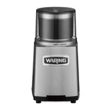 A stainless steel Waring WSG60KSDI Commercial Spice Grinder with a clear plastic top, labeled “Waring” on the front. The brushed metal finish and lock/unlock symbols beneath the transparent lid make it ideal for international use.