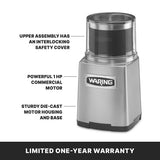 A silver Waring WSG60KSDI Commercial Spice Grinder features an interlocking safety cover, a powerful 1 HP commercial motor, and a sturdy die-cast housing; text below reads “Limited One-Year Warranty” on a black background. Suitable for international use.