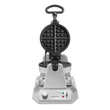 A stainless steel, commercial Belgian Waffle Maker with a round, open waffle grid, a top handle, control dial, and indicator lights on a rectangular base. The heavy-duty waffle maker faces forward with its grilling plates open.