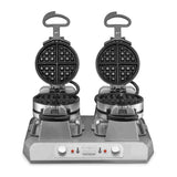 A commercial Belgian waffle maker with quad side-by-side round non-stick plates is open, revealing the grids. The sturdy, rectangular “Waring” base has two control knobs, indicator lights, and raised black handles.