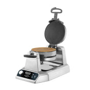 A stainless steel Waring waffle maker with non-stick plates and a round, textured cooking surface is open, revealing a golden-brown waffle inside. It features a handle, digital controls, and a drip tray at the base.