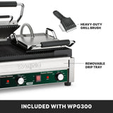 A stainless steel dual panini grill with cast iron plates, a closed handle, removable drip tray, and control knobs is shown. A heavy-duty grill brush is pictured above it. Text reads: “INCLUDED WITH WPG300”—“HEAVY-DUTY GRILL BRUSH”—“REMOVABLE DRIP TRAY.”.