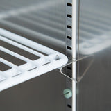 Close-up of a white wire shelf installed on a metallic shelving unit inside a commercial refrigerator. The shelf is supported by a metal bracket slotted into vertical rails, which feature evenly spaced holes for adjustable placement.